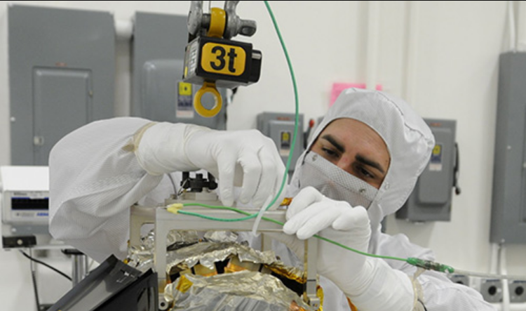 A technician in a clean suit inspects wiring on spacecraft component